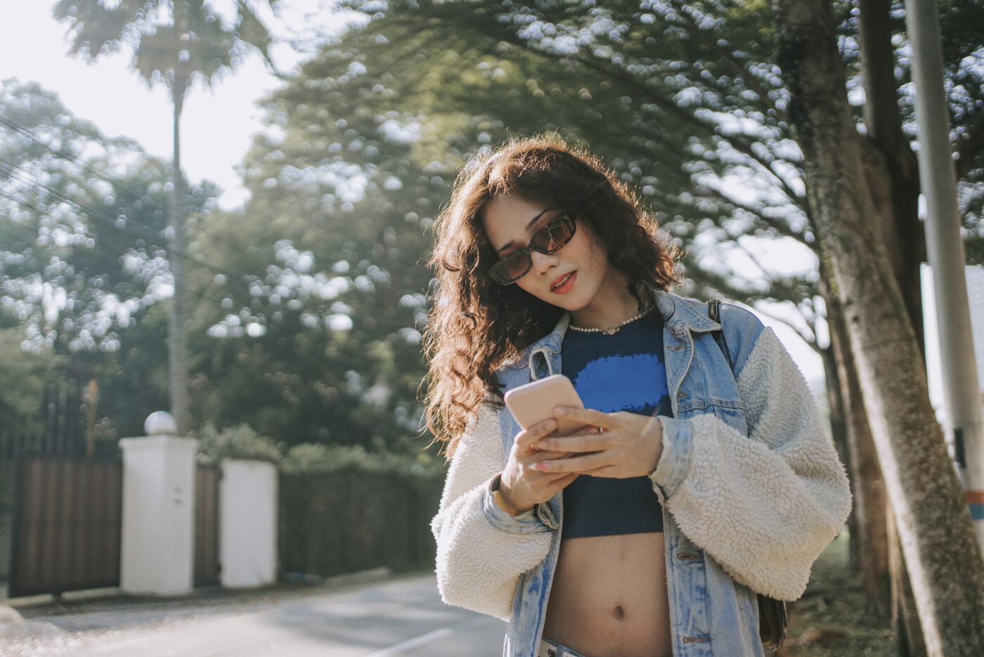 Gen Z female reading text messages with smart phone on the street in the morning