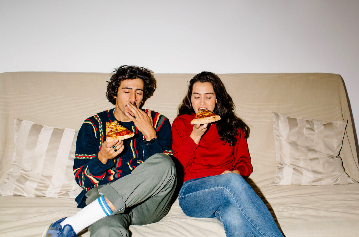 Gen Zers sitting on sofa at home and enjoying pizza.