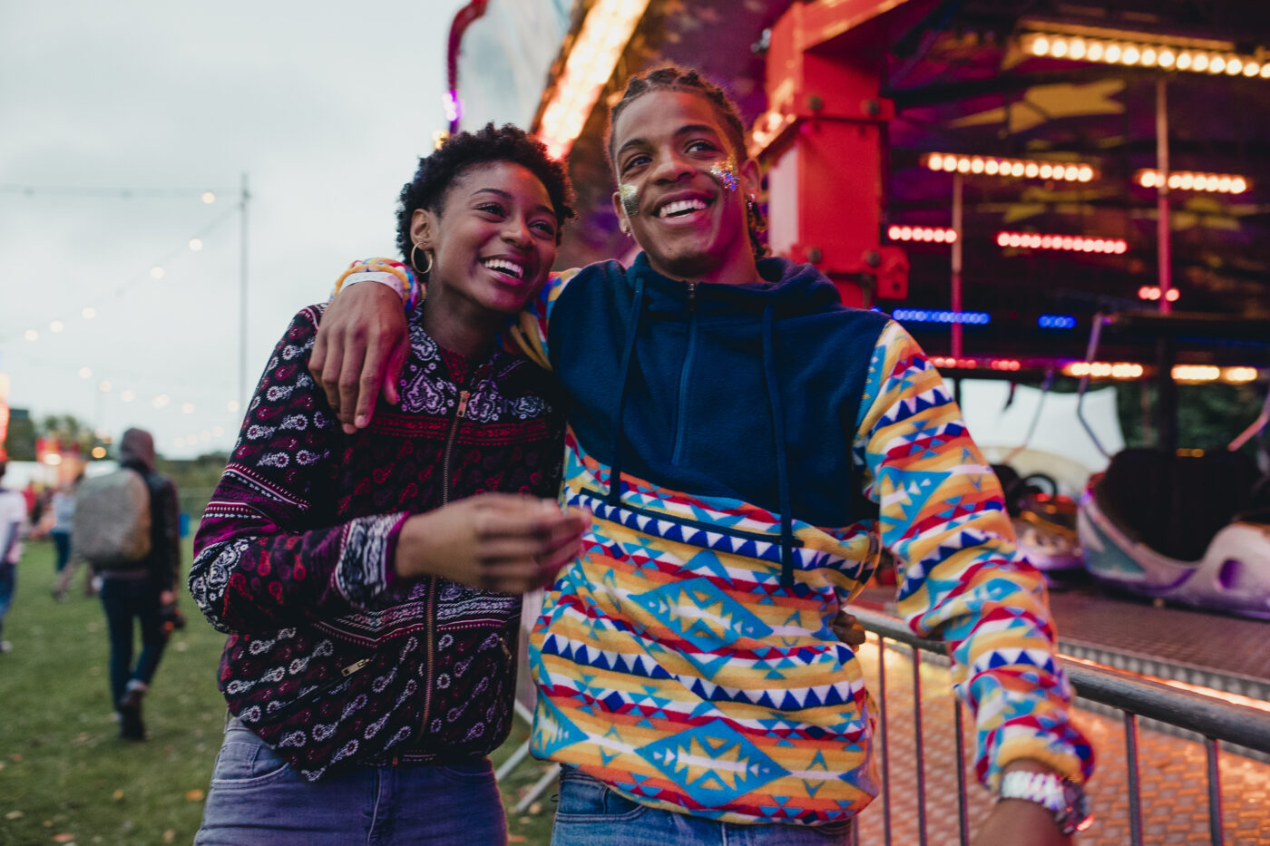 Young Gen Z couple are laughing and talking as they walk around a funfair.